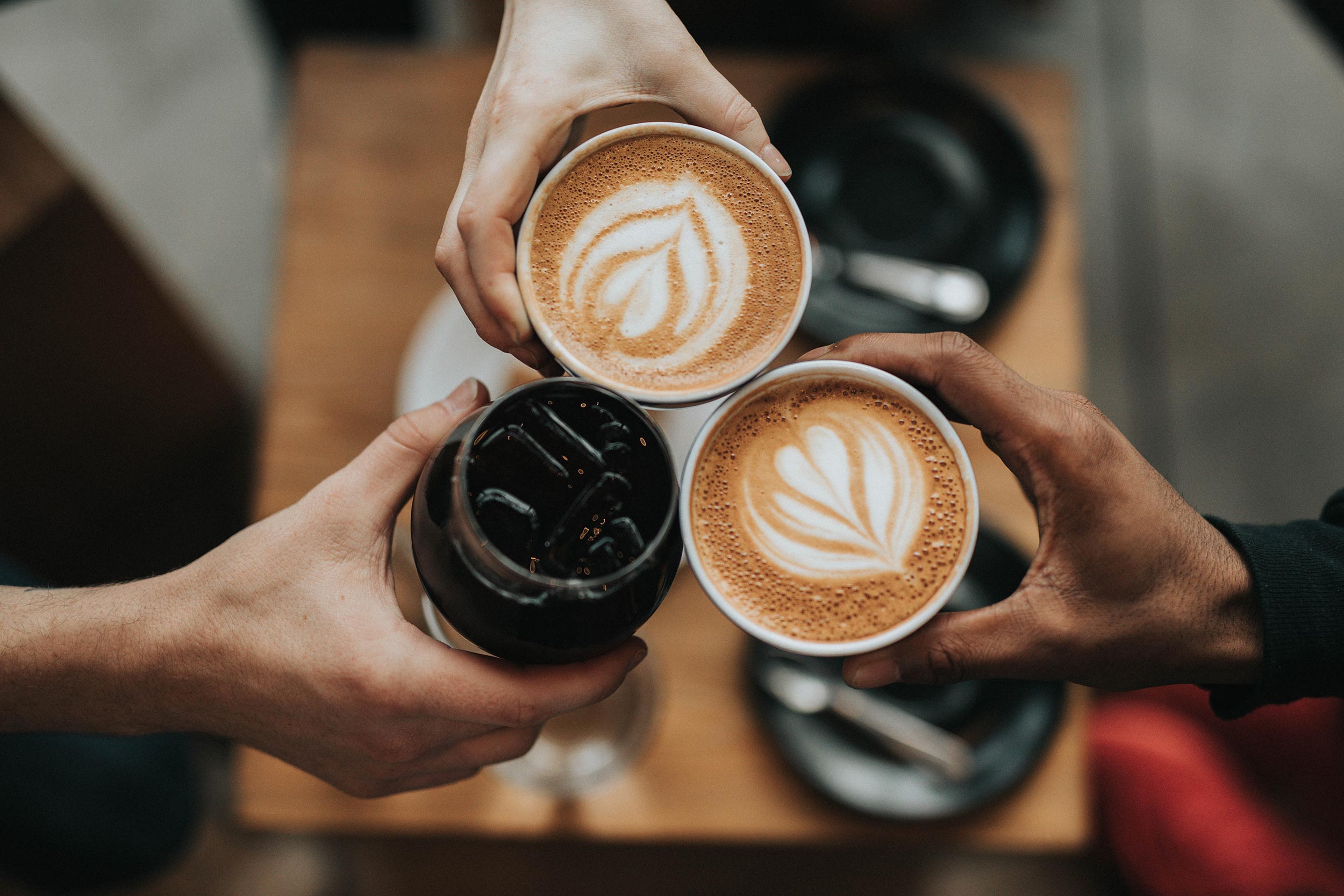 Hands toasting with paper cups and lattes from above, showing latte art